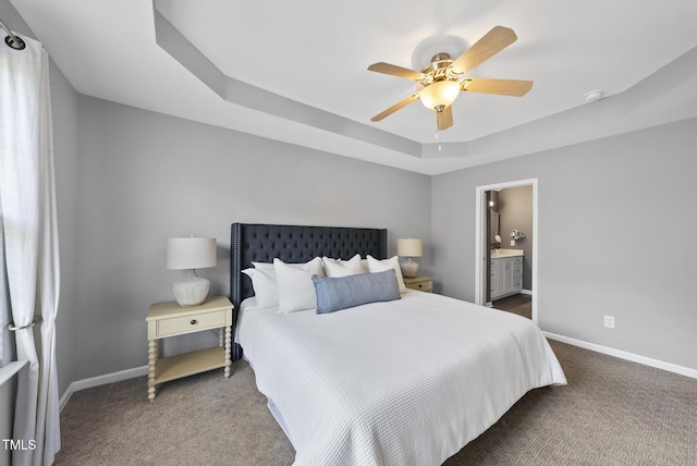 bedroom with ensuite bathroom, baseboards, a raised ceiling, a ceiling fan, and carpet flooring