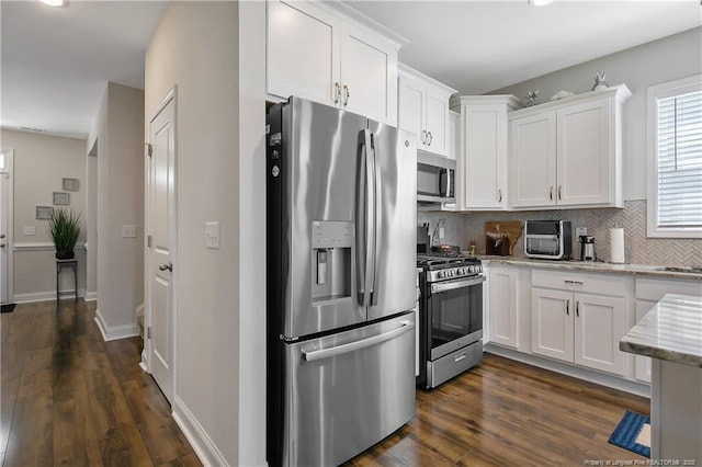 kitchen featuring dark wood finished floors, white cabinets, appliances with stainless steel finishes, light stone counters, and decorative backsplash