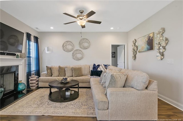 living area featuring ceiling fan, dark wood-type flooring, a fireplace with raised hearth, recessed lighting, and baseboards