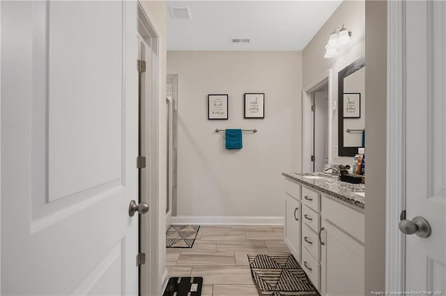 bathroom with visible vents, baseboards, a sink, a shower, and double vanity