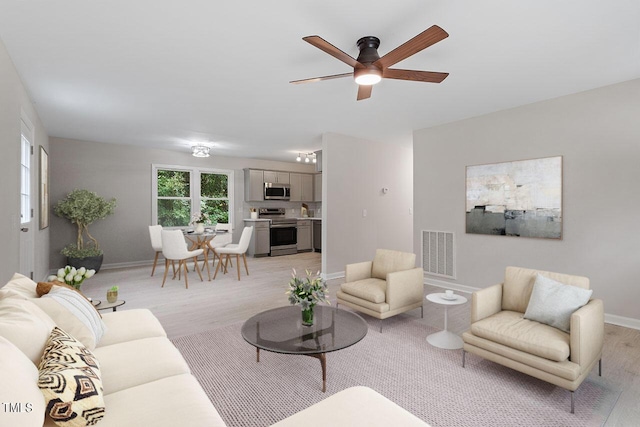 living area featuring baseboards, a ceiling fan, visible vents, and light wood-style flooring