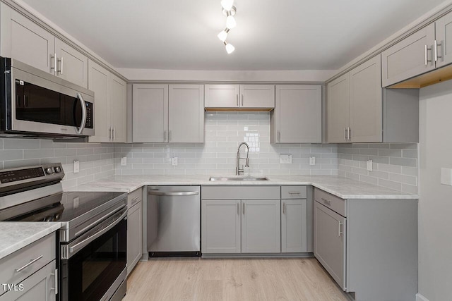 kitchen featuring tasteful backsplash, a sink, gray cabinets, light wood finished floors, and appliances with stainless steel finishes