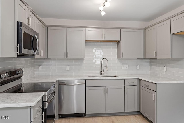 kitchen featuring stainless steel appliances, gray cabinetry, a sink, and backsplash