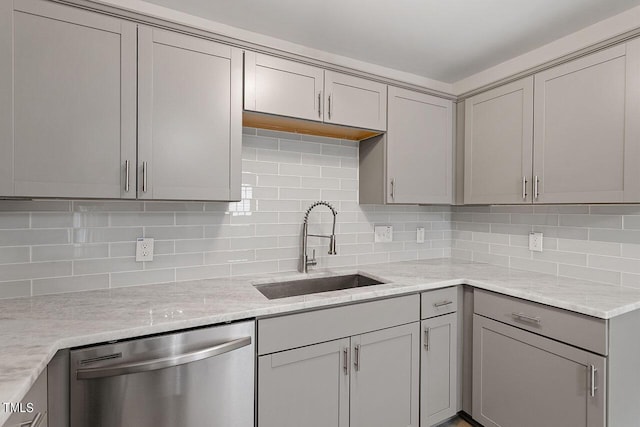 kitchen with light stone counters, backsplash, dishwasher, a sink, and gray cabinetry