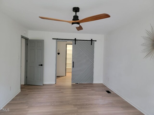 spare room featuring a ceiling fan, a barn door, wood finished floors, and baseboards