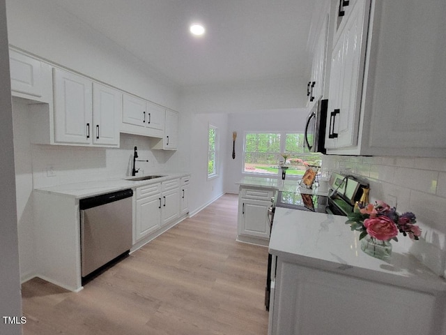 kitchen featuring appliances with stainless steel finishes, a sink, white cabinets, tasteful backsplash, and light wood-style flooring