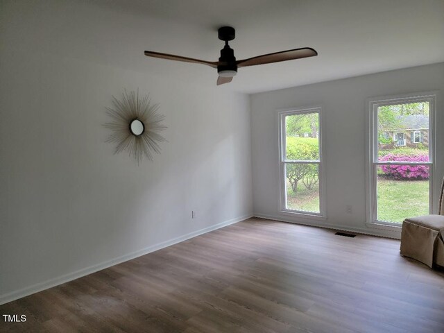 empty room with a ceiling fan, plenty of natural light, and wood finished floors