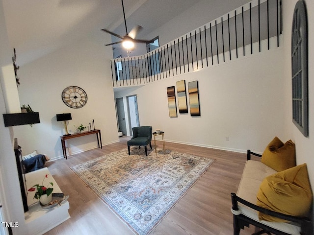 living area with a ceiling fan, wood finished floors, baseboards, and high vaulted ceiling