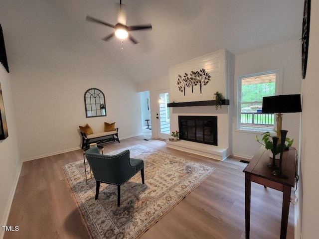 living area featuring ceiling fan, wood finished floors, a glass covered fireplace, baseboards, and high vaulted ceiling