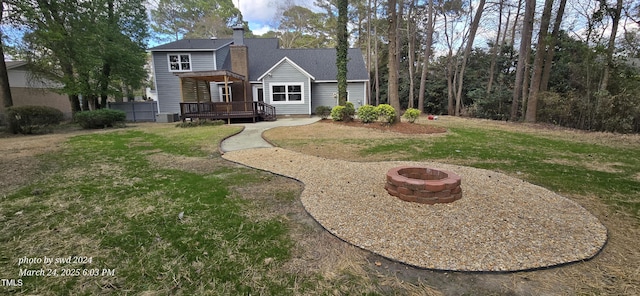 rear view of house with an outdoor fire pit, a wooden deck, a lawn, and a chimney