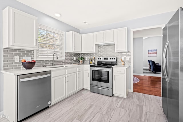 kitchen with white cabinetry, light countertops, a sink, stainless steel appliances, and decorative backsplash