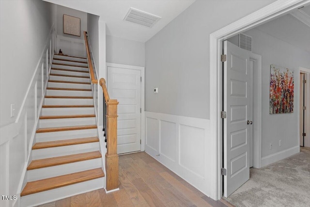 staircase featuring wood finished floors, a decorative wall, visible vents, and a wainscoted wall