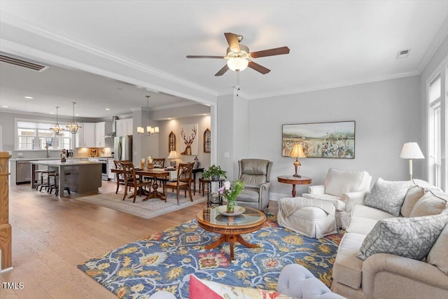 living area featuring light wood-style flooring, ceiling fan with notable chandelier, visible vents, and crown molding