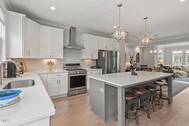 kitchen with a notable chandelier, ornamental molding, wall chimney range hood, appliances with stainless steel finishes, and a sink