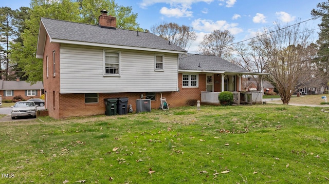 rear view of property featuring a yard, central AC unit, brick siding, and a chimney
