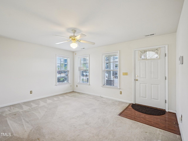 carpeted foyer featuring ceiling fan and baseboards