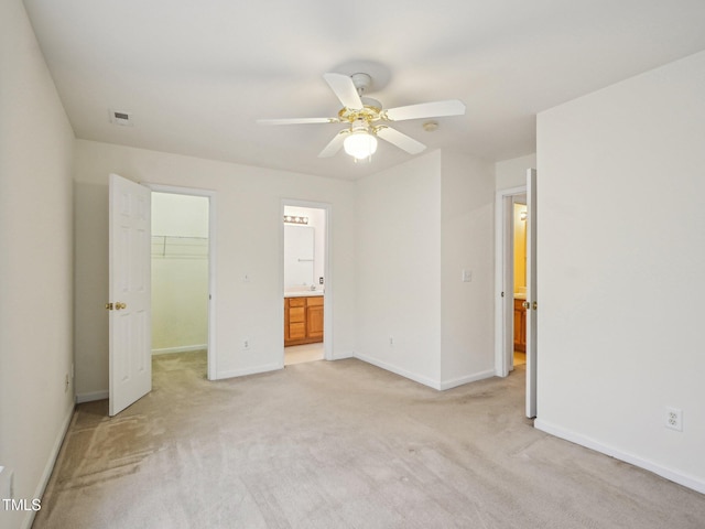 unfurnished bedroom with light carpet, a spacious closet, baseboards, a closet, and ensuite bath