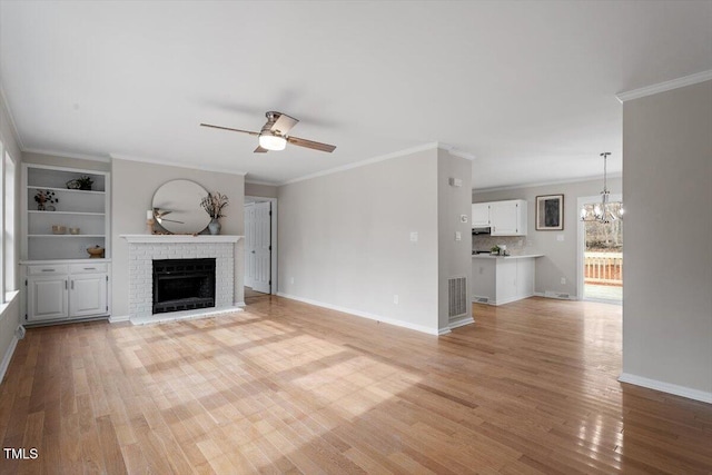 unfurnished living room with visible vents, a brick fireplace, light wood-style floors, crown molding, and ceiling fan with notable chandelier