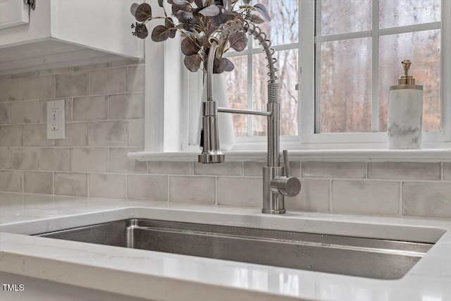 details featuring a sink, white cabinets, tasteful backsplash, and light stone countertops