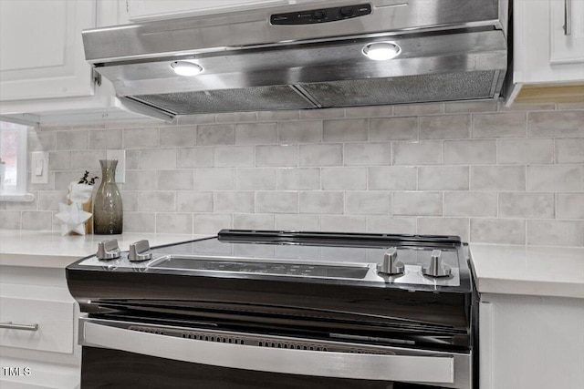 kitchen with white cabinets, under cabinet range hood, tasteful backsplash, and light countertops