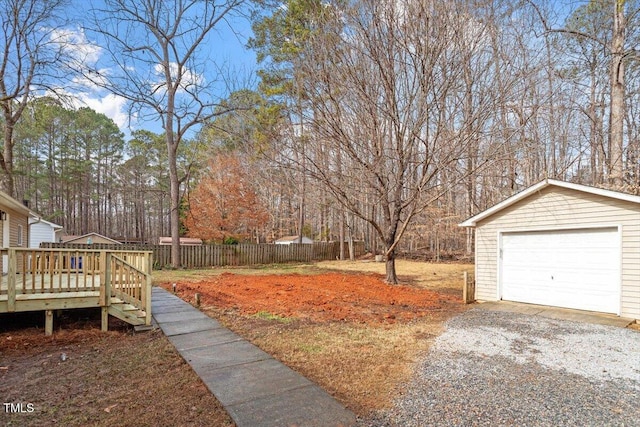 view of yard with a detached garage, fence, an outbuilding, a wooden deck, and driveway