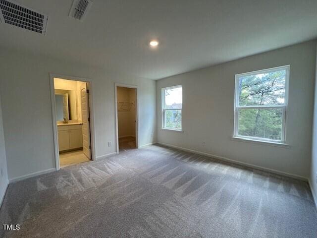 unfurnished bedroom featuring light carpet, baseboards, multiple windows, and visible vents