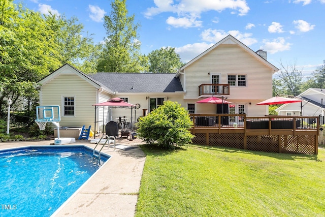 rear view of house featuring a lawn, a wooden deck, an outdoor pool, and a hot tub