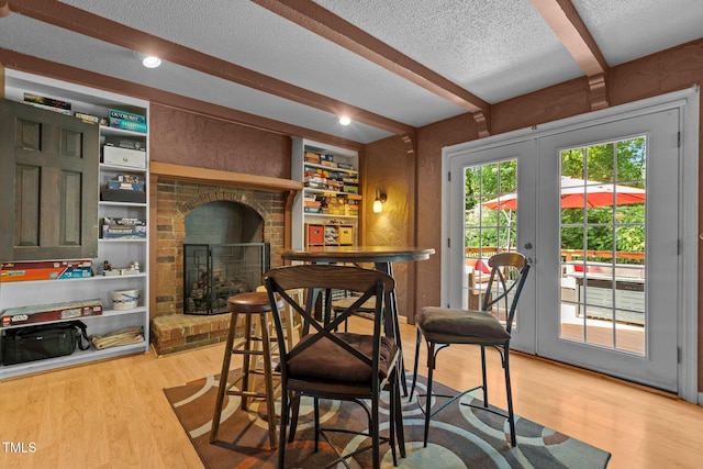 dining space with a textured ceiling, light wood-style floors, french doors, a fireplace, and beamed ceiling