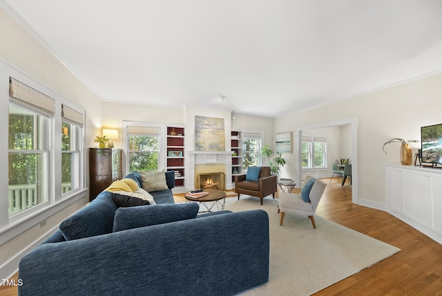 living room featuring baseboards, ornamental molding, wood finished floors, and a lit fireplace