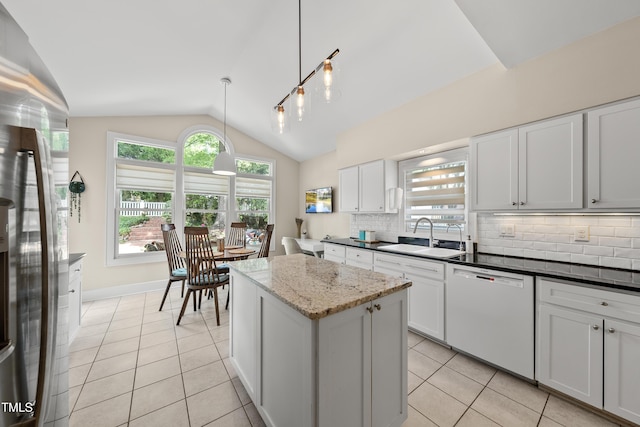 kitchen with backsplash, white dishwasher, vaulted ceiling, a sink, and freestanding refrigerator