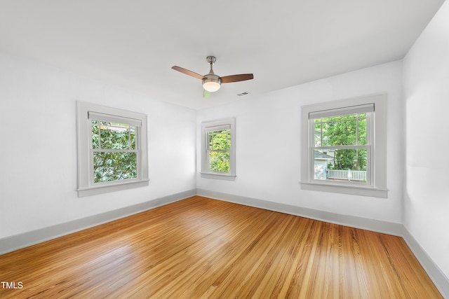 spare room featuring baseboards, light wood finished floors, and a wealth of natural light