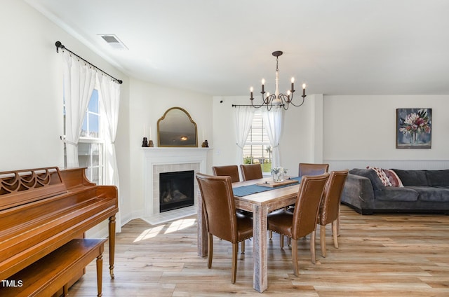 dining room featuring a fireplace, a notable chandelier, light wood finished floors, and visible vents