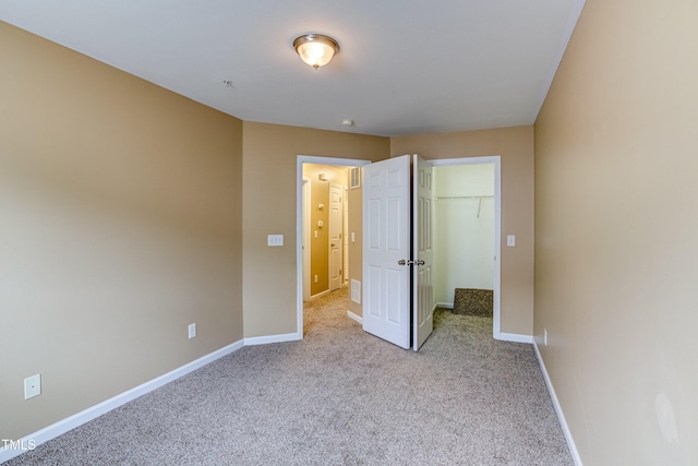 unfurnished bedroom with a closet, a walk in closet, baseboards, and carpet floors