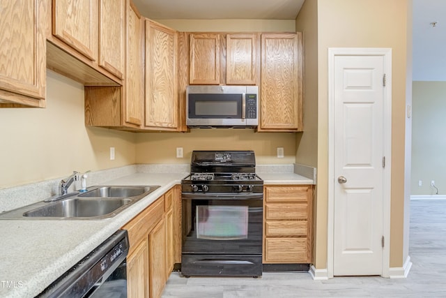 kitchen with baseboards, light countertops, black appliances, a sink, and light brown cabinetry