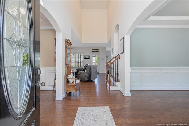 foyer entrance with arched walkways, dark wood-type flooring, wainscoting, and crown molding