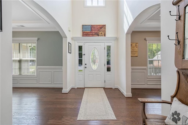 foyer featuring dark wood-type flooring, arched walkways, and ornamental molding