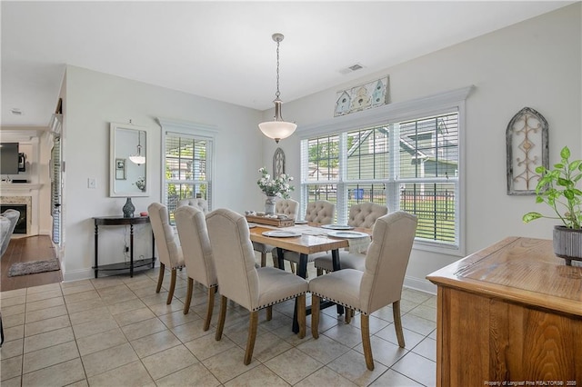 dining space with light tile patterned floors, baseboards, visible vents, and a fireplace
