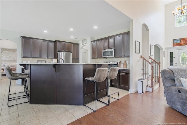 kitchen featuring arched walkways, a breakfast bar, appliances with stainless steel finishes, dark brown cabinetry, and decorative backsplash