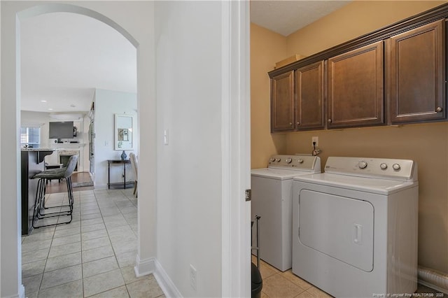 laundry area with light tile patterned floors, arched walkways, separate washer and dryer, baseboards, and cabinet space