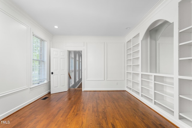 spare room with ornamental molding, wood finished floors, baseboards, built in shelves, and arched walkways