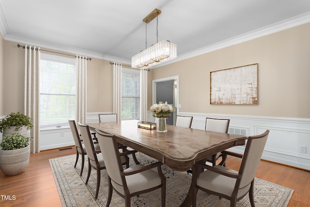 dining area with visible vents, wainscoting, wood finished floors, an inviting chandelier, and ornamental molding