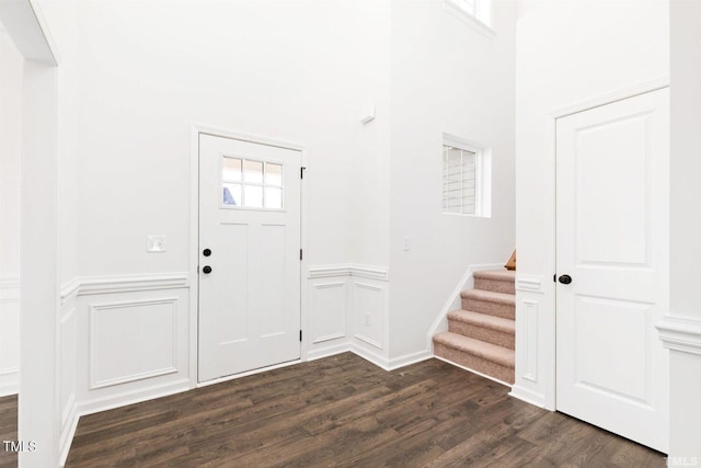 entrance foyer featuring dark wood-type flooring, a wainscoted wall, a decorative wall, and stairs