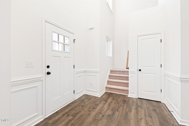 entryway featuring dark wood-style flooring, stairway, a decorative wall, and wainscoting
