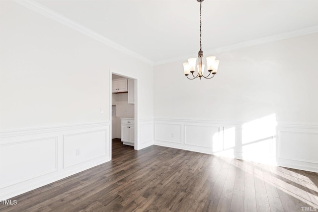unfurnished dining area featuring dark wood-type flooring, ornamental molding, a wainscoted wall, and a notable chandelier