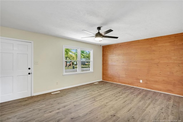 3014 Akron Dr, Hope Mills, NC 28348 - spare room featuring baseboards, wooden walls, a textured ceiling, a ceiling fan, and wood finished floors