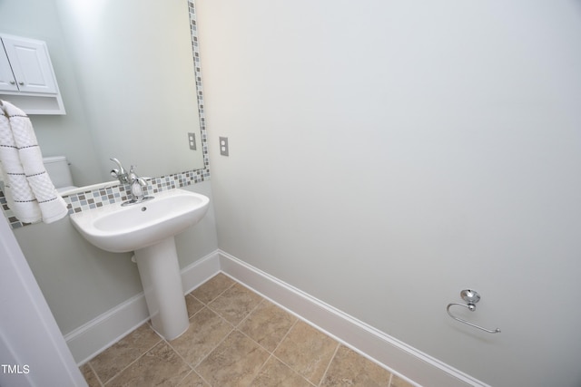 half bathroom featuring a sink, baseboards, and backsplash