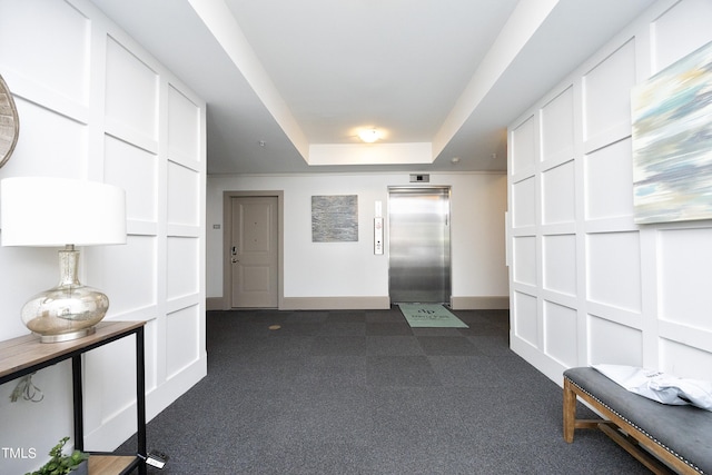 corridor with dark carpet, elevator, baseboards, and a raised ceiling