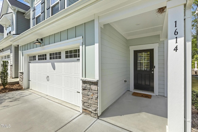 view of exterior entry featuring an attached garage, board and batten siding, driveway, and stone siding