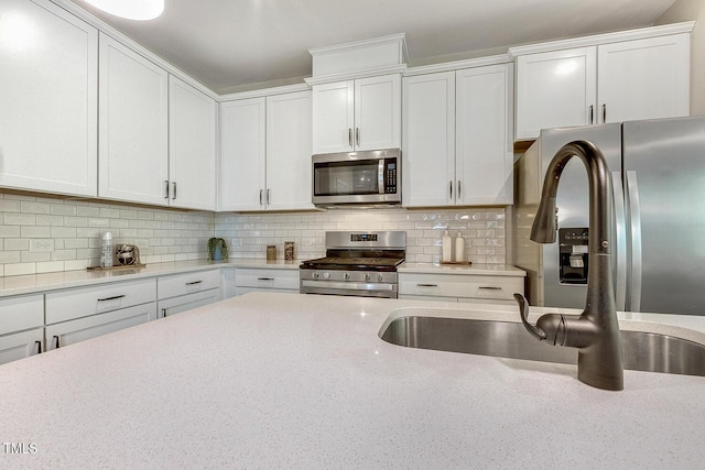 kitchen featuring white cabinets, a sink, stainless steel appliances, backsplash, and light stone counters