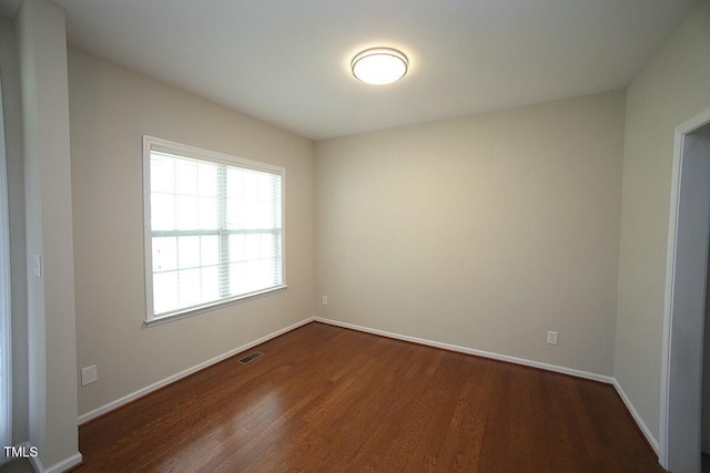 spare room featuring visible vents, baseboards, and dark wood finished floors